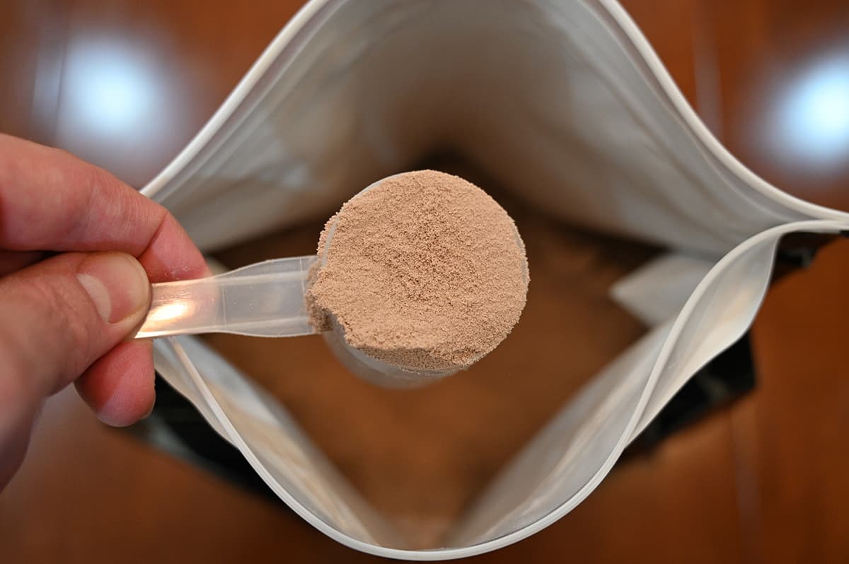 Top down image of a scoop of chocolate whey protein powder hovering over top an open bag.