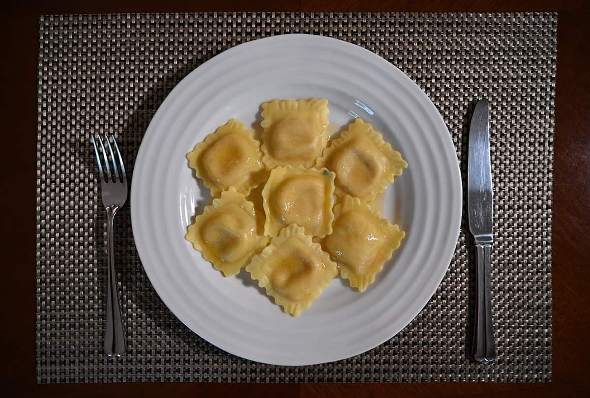Top down image of seven cooked ravioli served on a white plate. Beside the ravioli is a fork and knife.