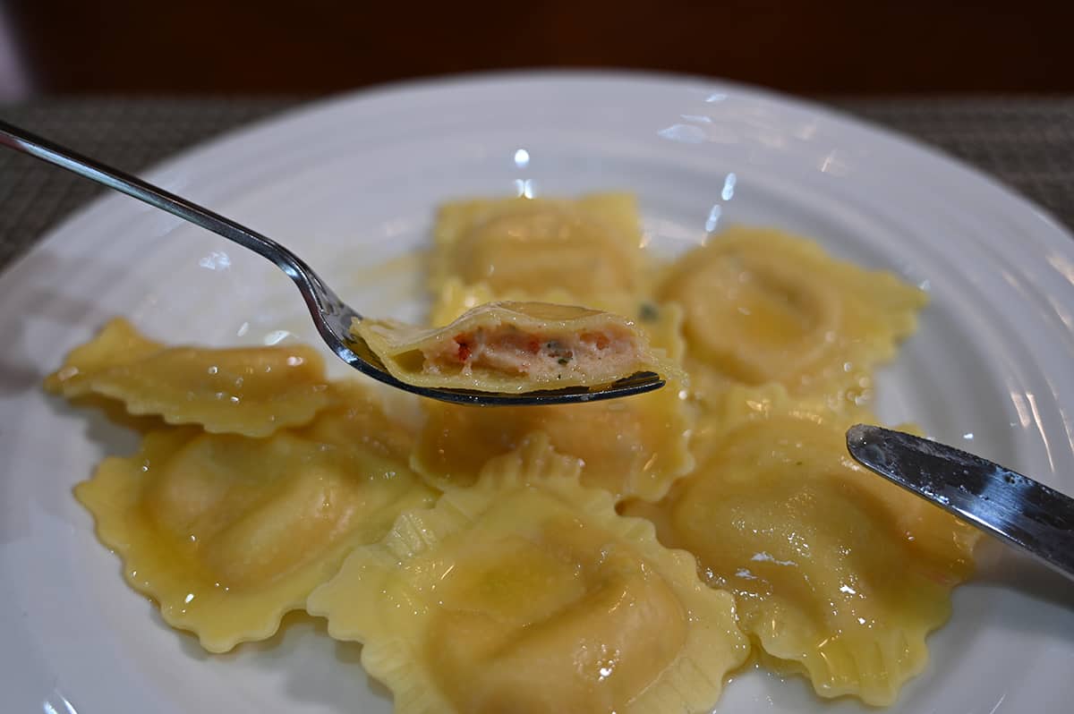 Side view image of a ravioli on a fork close to the camera that's been cut in half so you can see the filling inside the ravioli.
