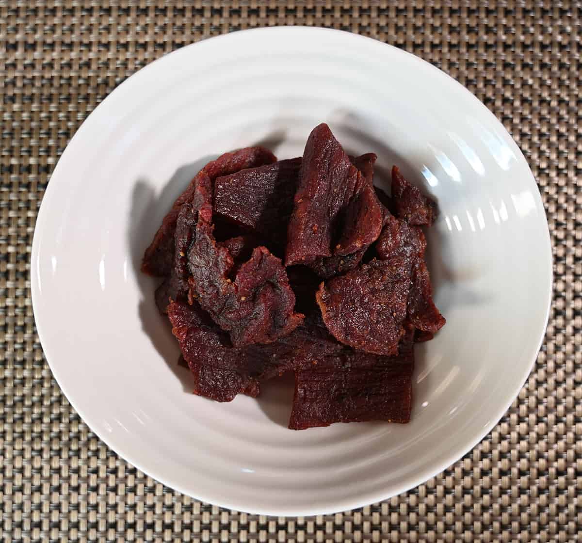 Top down image of a white bowl full of pieces of beef jerky.