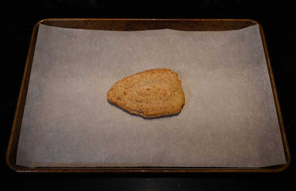 Top down image of one uncooked stuffed chicken breast sitting on a parchment paper lined baking tray ready to go in the oven.