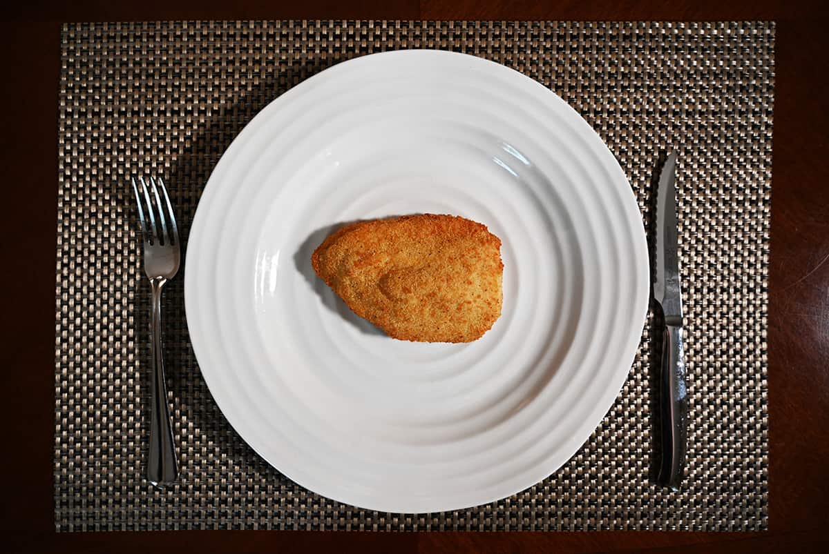 Top down image of one breaded stuffed chicken breast cooked and served on a white plate.