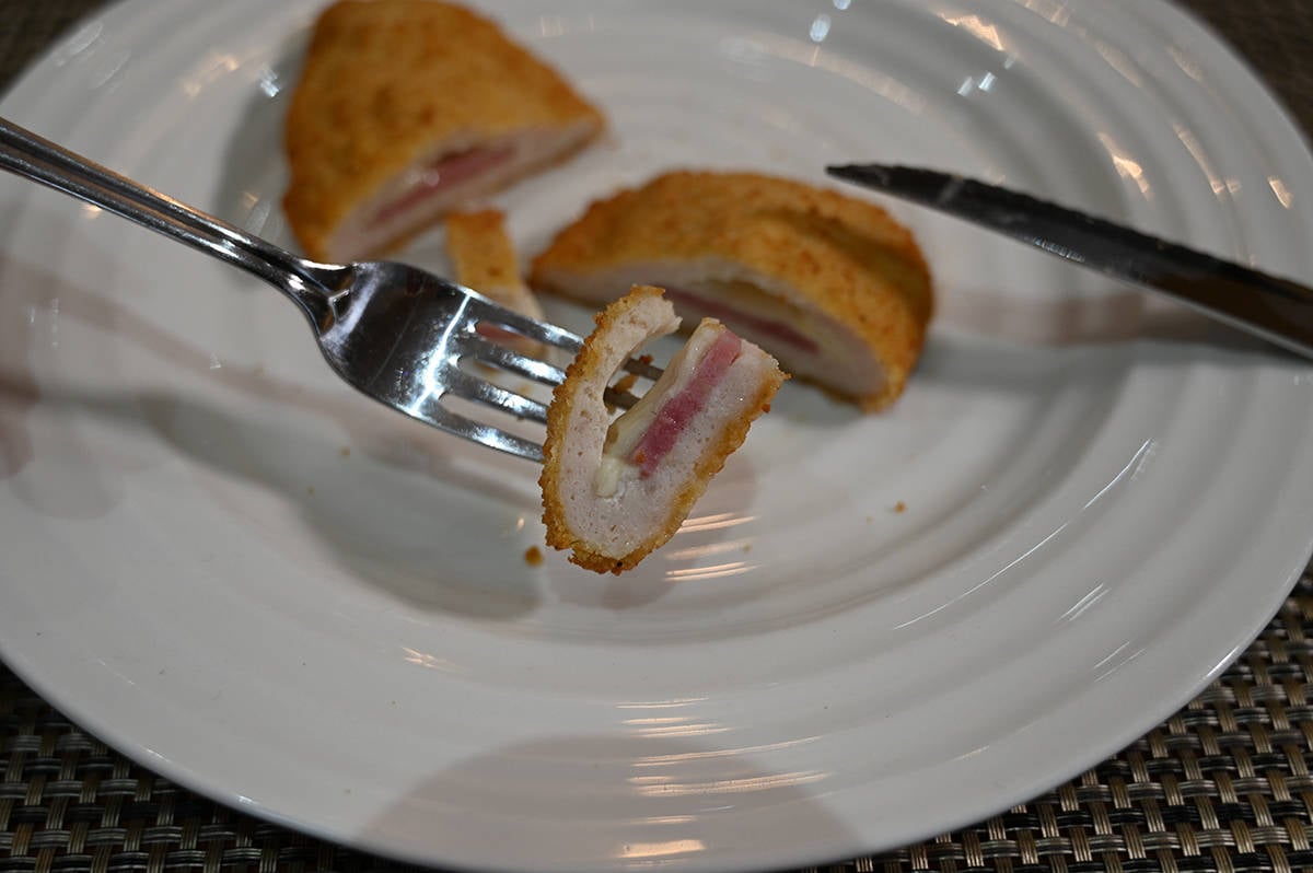 Side view closeup image of a fork with a cut piece of stuffed chicken breast on it so you can see the chicken, cheese and ham inside.