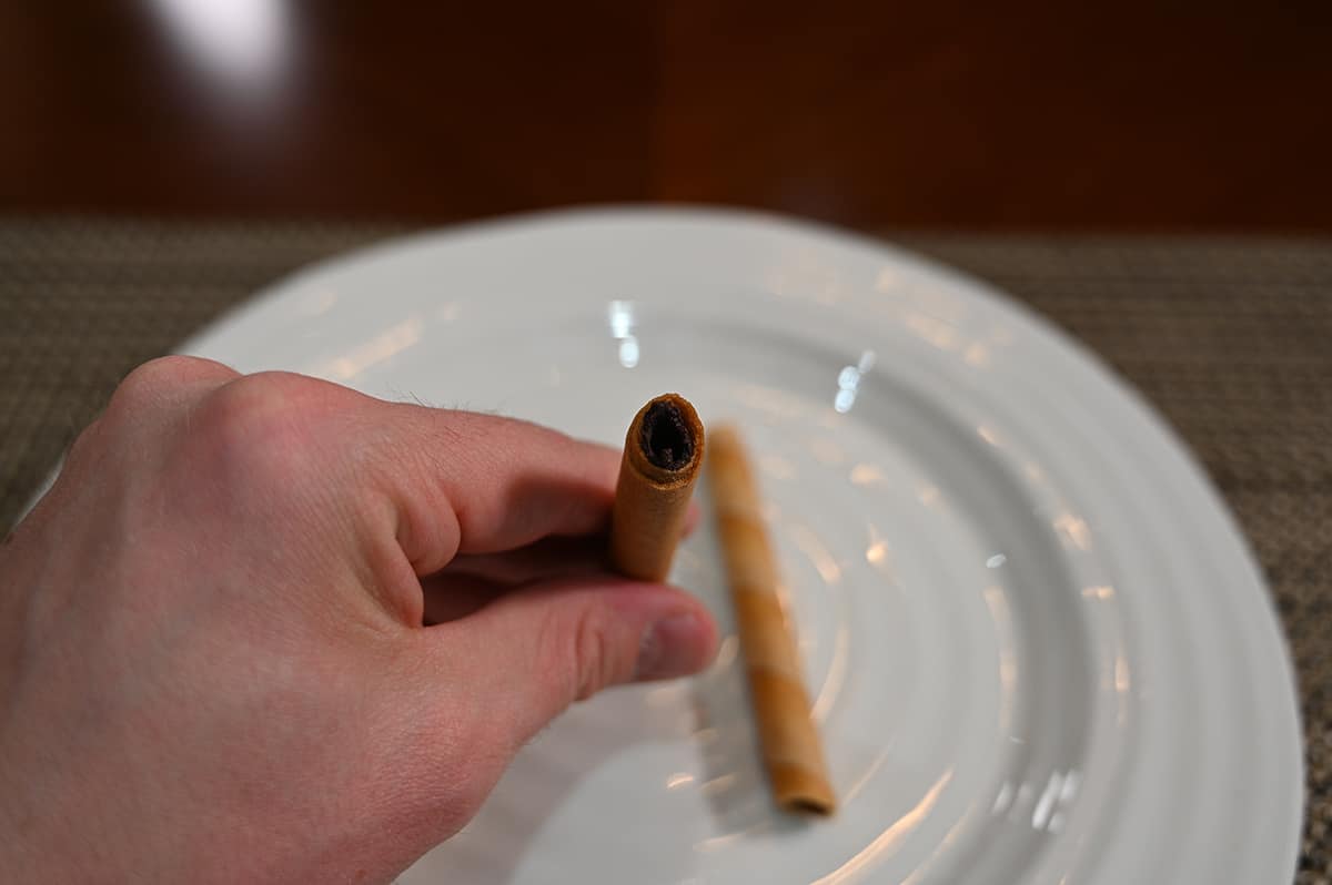 Top down image of a hand holding one chocolate rolled wafer up to the camera so you can see the filling inside.