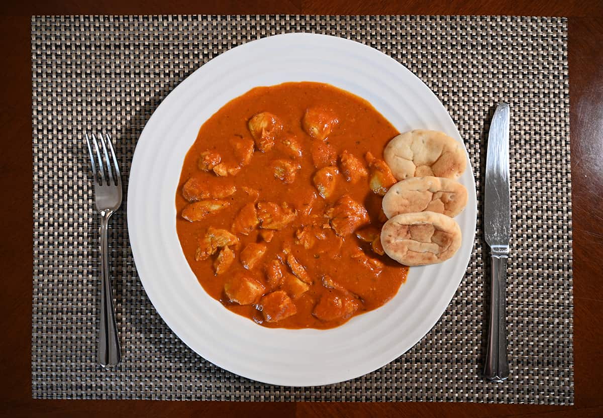 Top down image of a plate with chicken tikka masala on it served beside three mini naan.