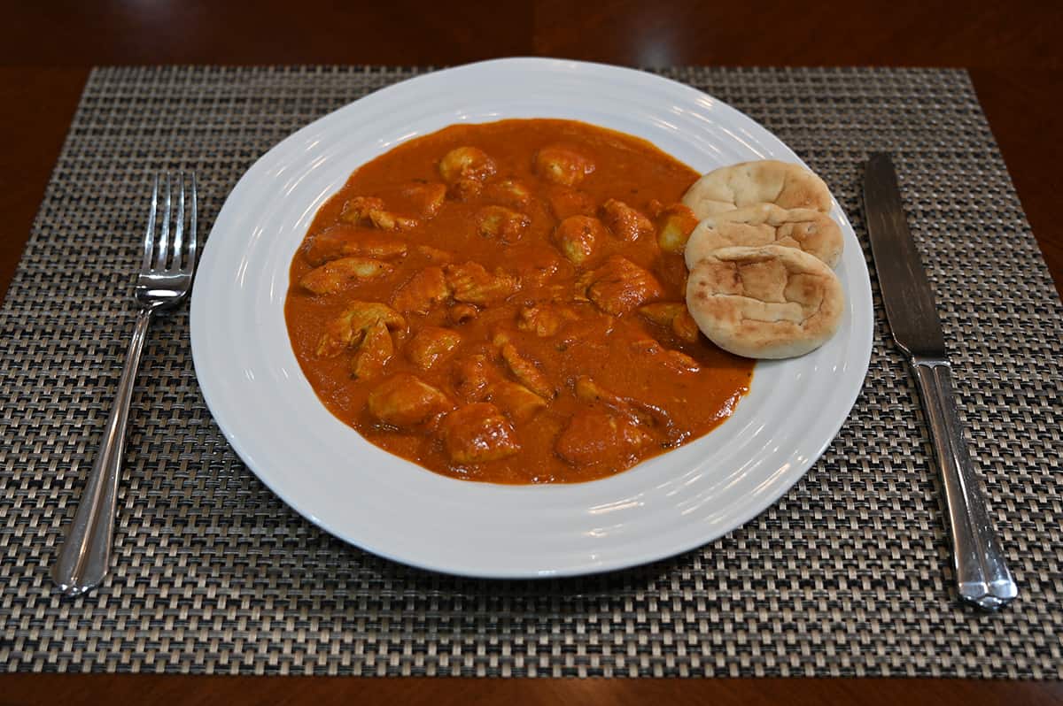 Sideview top image of a plate of chicken tikka masala served along mini naan.