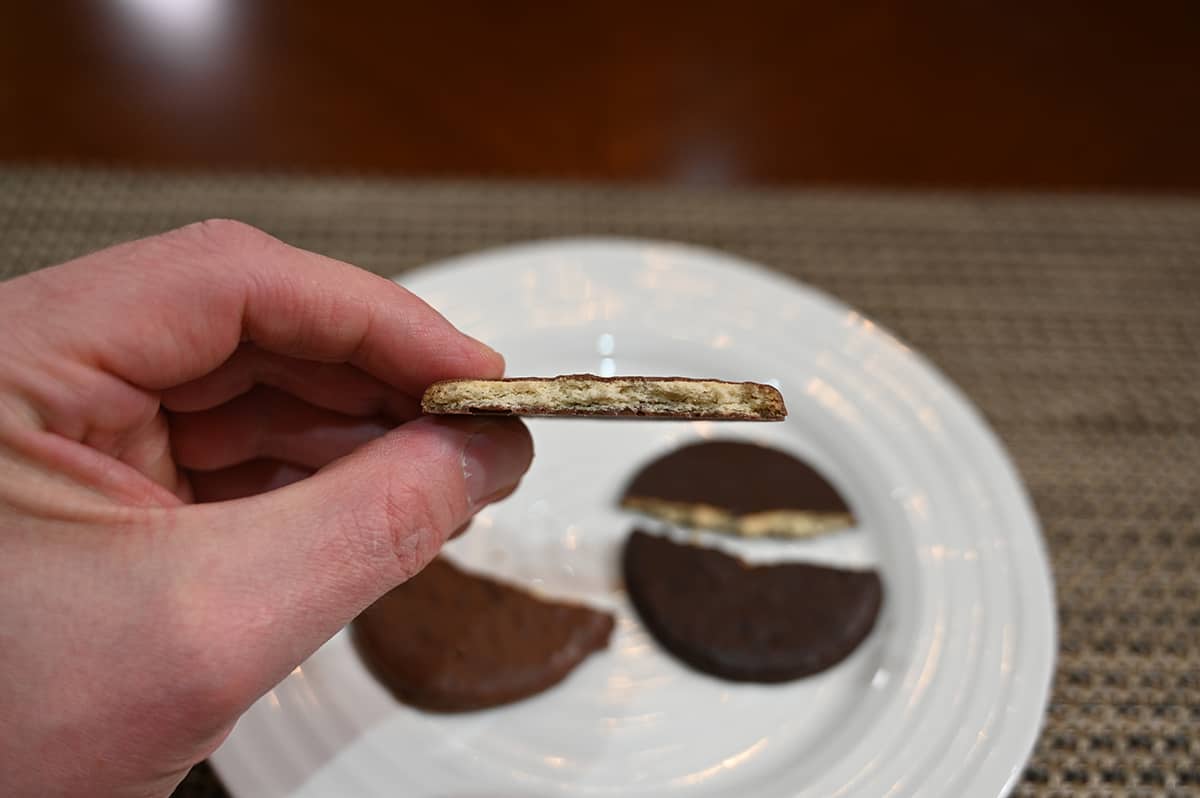 Closeup image of a hand holding a milk chocolate covered biscuit close to the camera with a few bites taken out so you can see the middle.