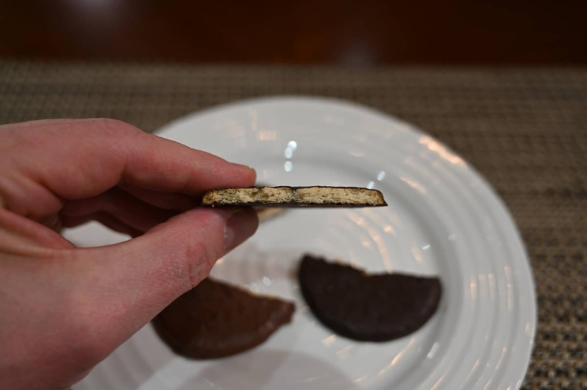 Closeup image of a hand holding a dark chocolate covered biscuit close to the camera with a few bites taken out so you can see the middle.