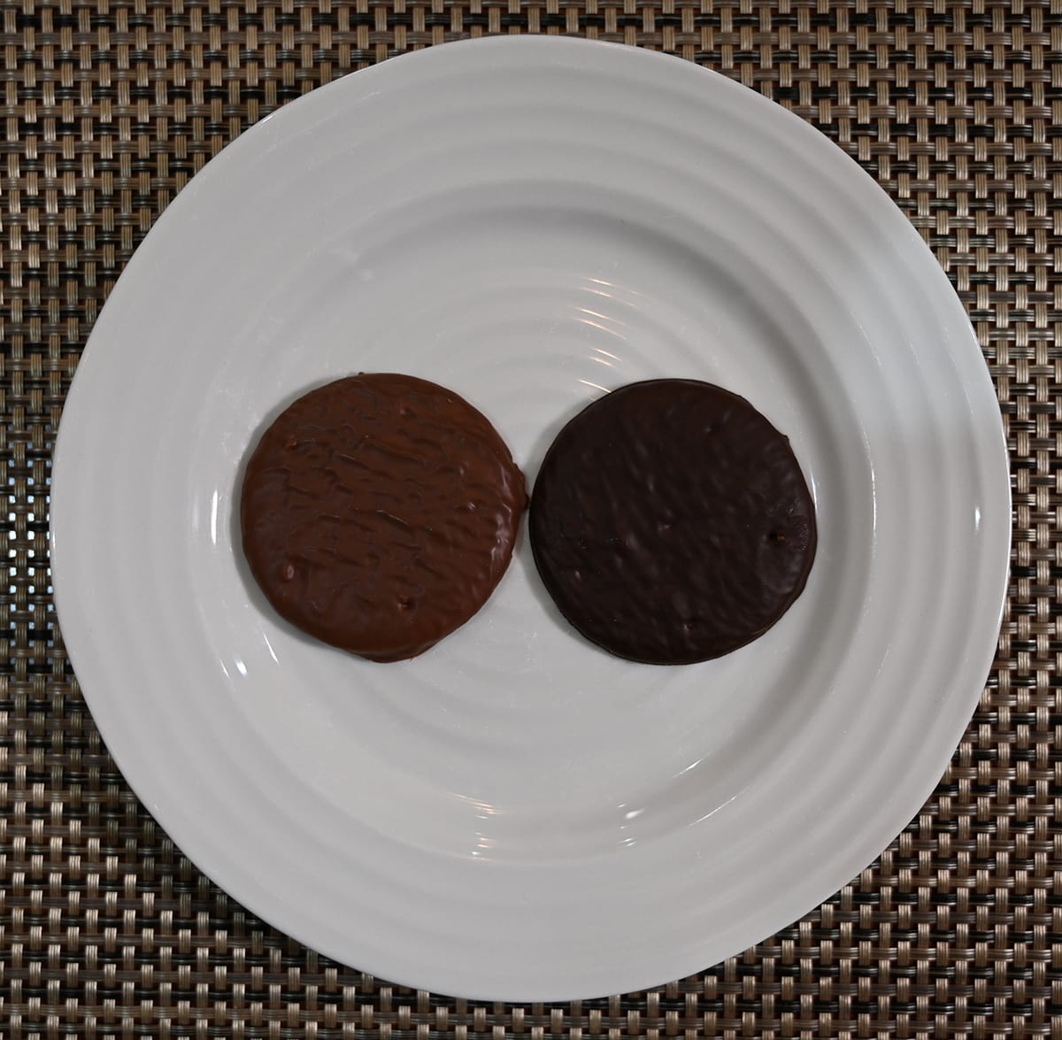 Top down image of a white plate with one milk chocolate butter biscuit beside a dark chocolate butter biscuit on it.