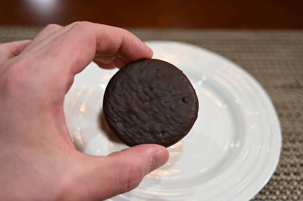 Closeup image of a hand holding a dark chocolate covered biscuit close to the camera.