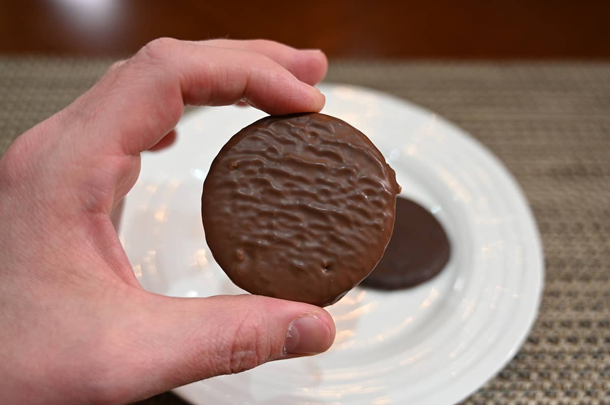 Closeup image of a hand holding a dark chocolate covered biscuit close to the camera.