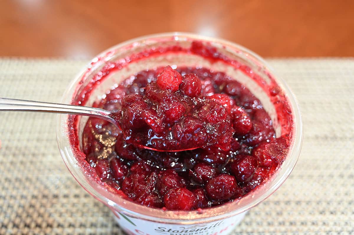 Sideview image of an open container of cranberry sauce and a spoon hovering over the container with sauce on the spoon.