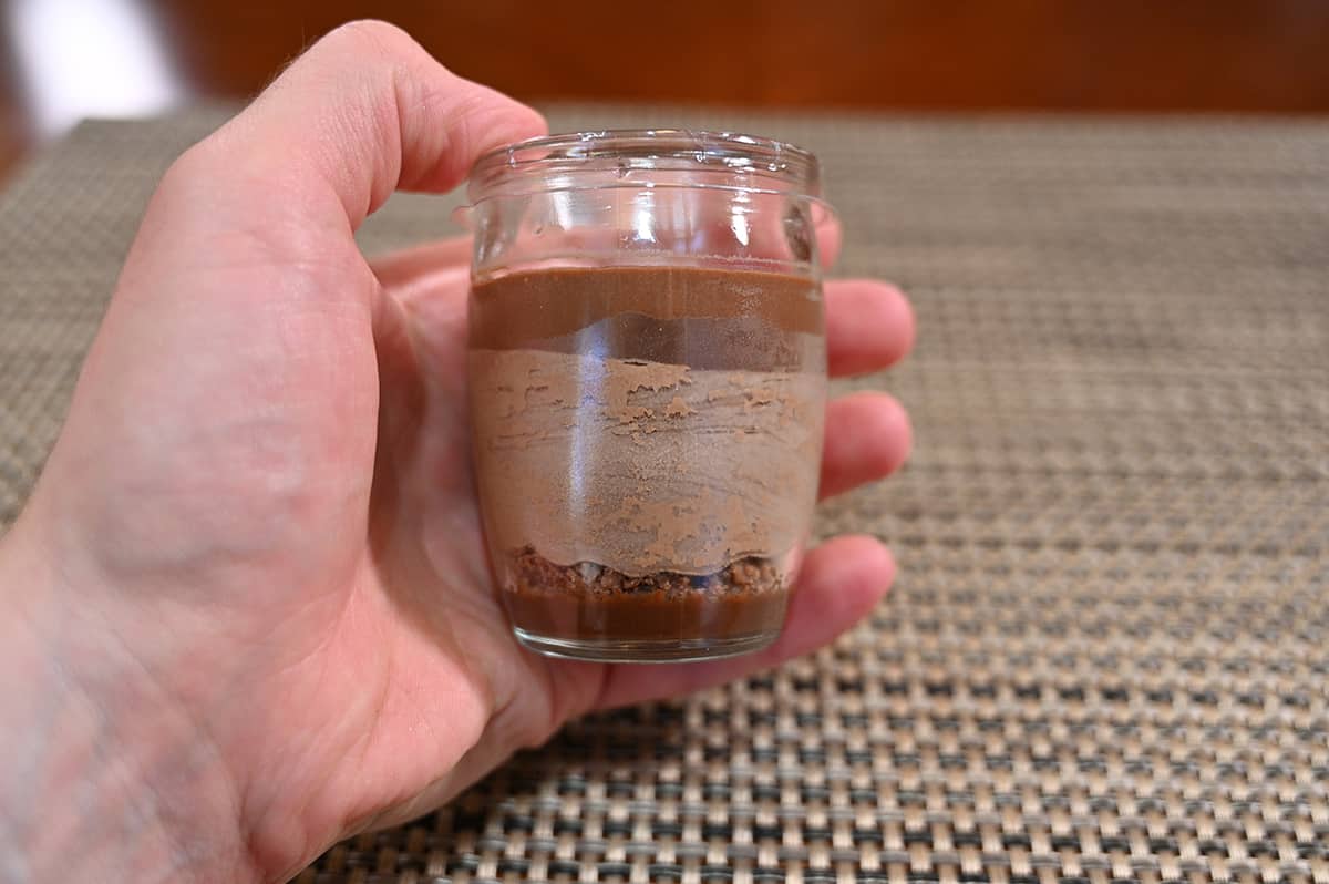 Closeup image of a hand holding one mousse cup unopened showing all the different layers in the cup.