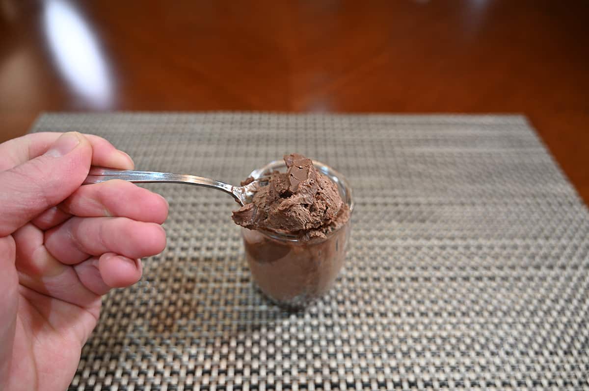 Sideview image of a hand with a spoon lifting mousse out of the cup showing the texture and appearance of the mousse. 