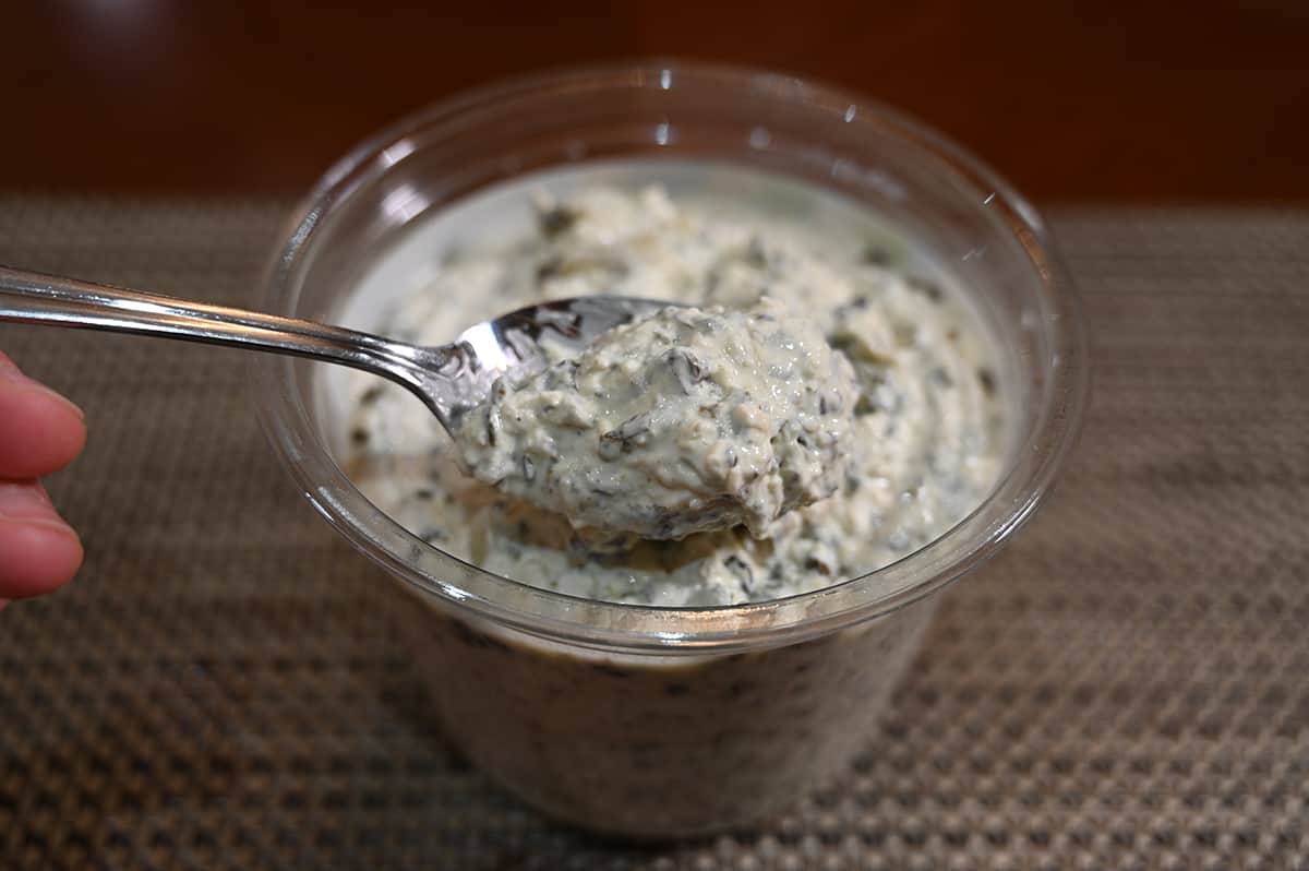 Sideview image of a spoon with dip on it hovering over the container of dip.