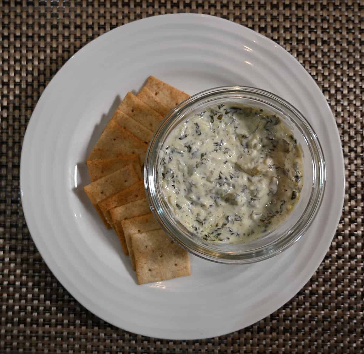 Top down image of the dip in a glass bowl on a white plate served beside crackers.