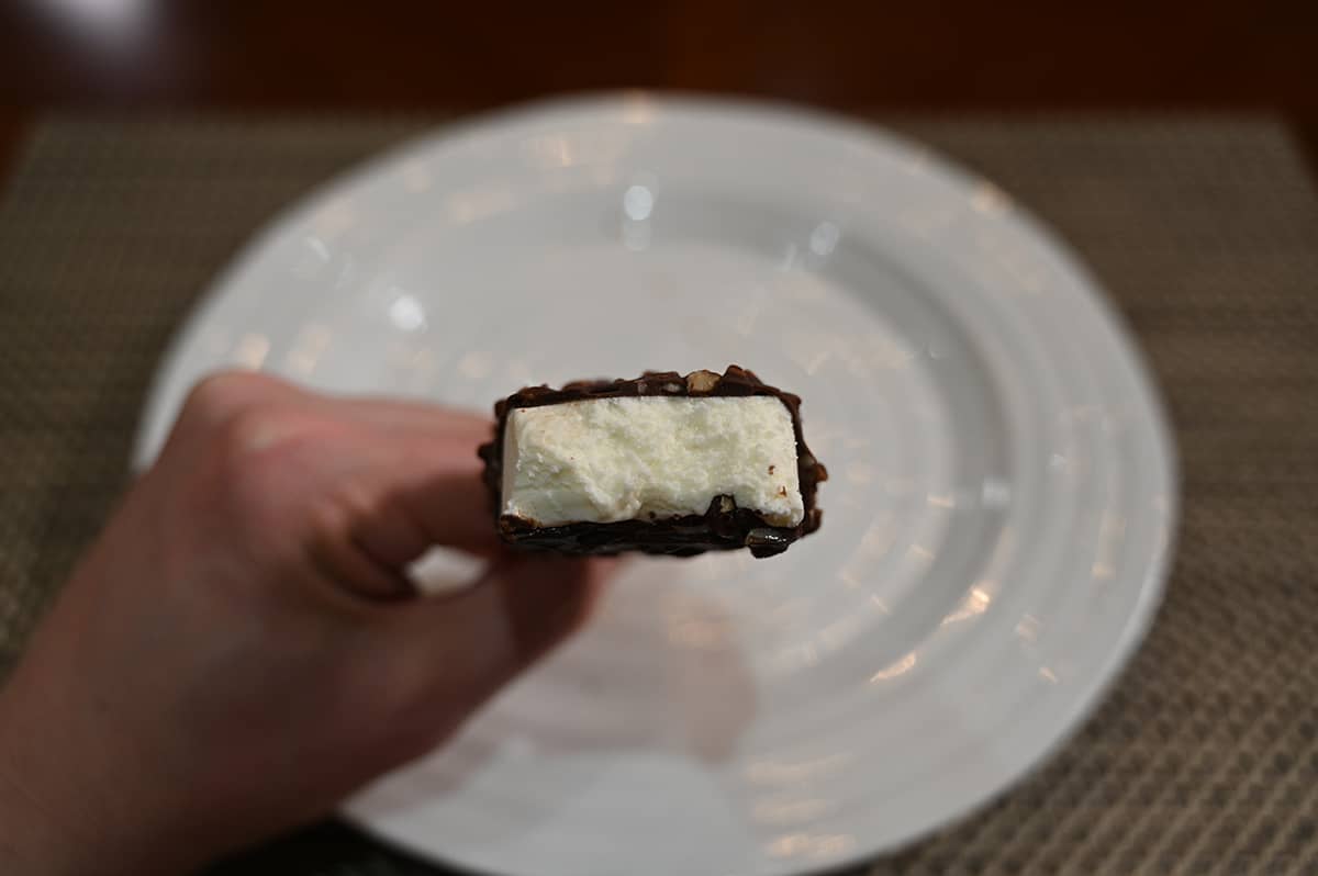 Closeup image of a hand holding an ice cream bar with a few bites taken out of it so you can see the center ice cream.