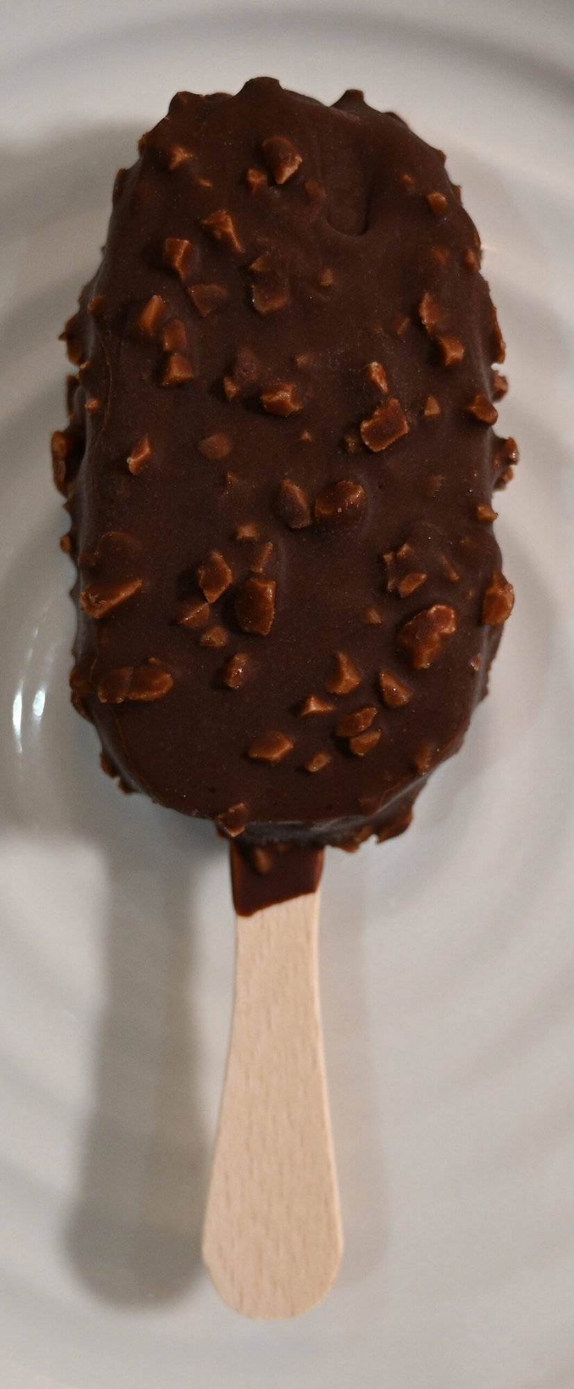 Very close image of one ice cream bar sitting on a plate unwrapped.