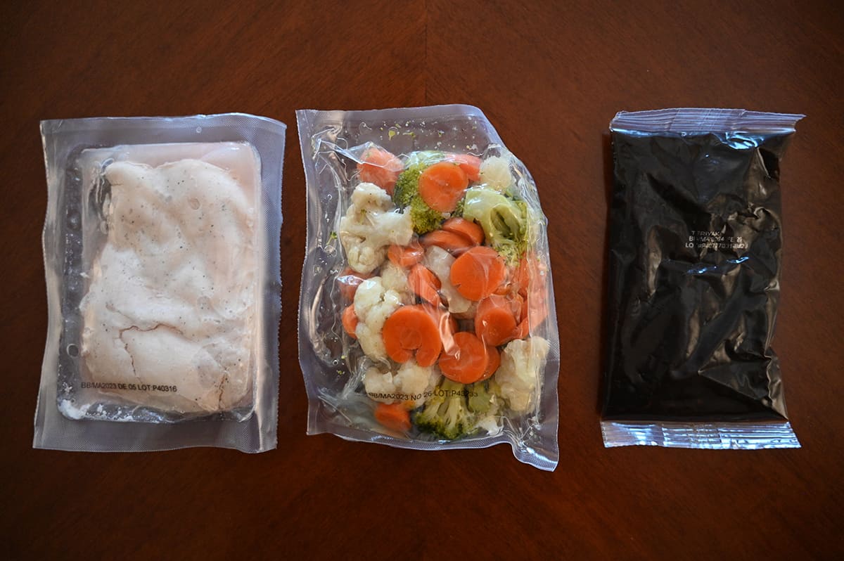 Top down image of pouches of chicken, vegetables and stir-fry sauce sitting on a table unopened.