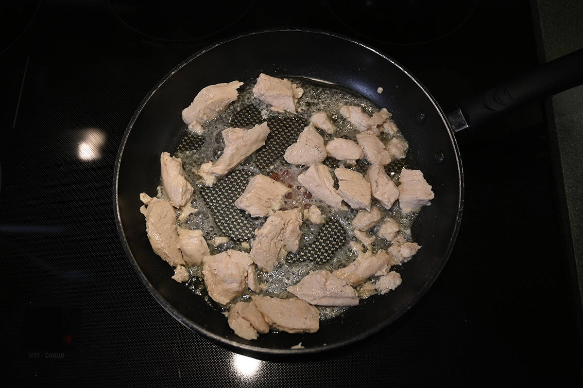 Image of chicken breast pieces heating in a pan on the stovetop with some oil in the pan.
