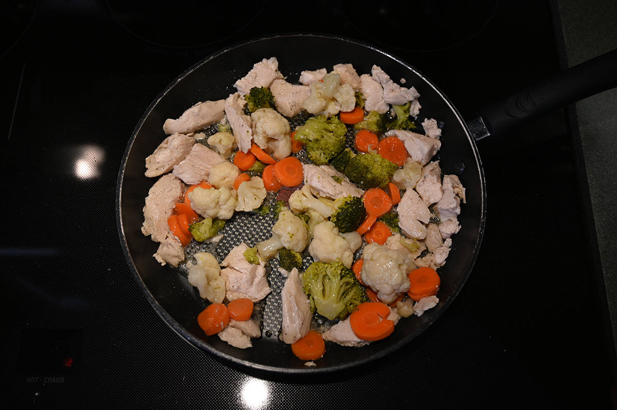 Image of chicken breast pieces and vegetables heating in a pan on the stovetop with some oil in the pan.