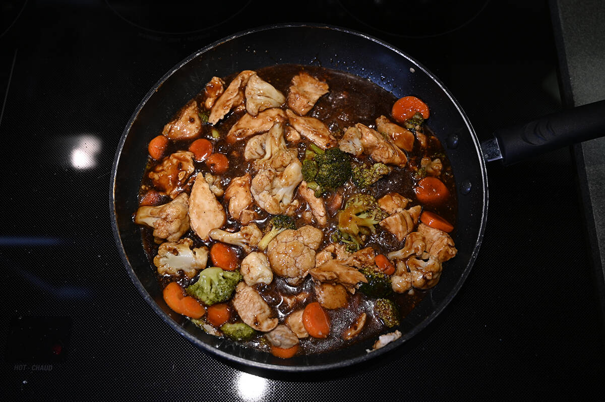 Image of chicken breast pieces, vegetables and sauce heating in a pan on the stovetop with some oil in the pan.