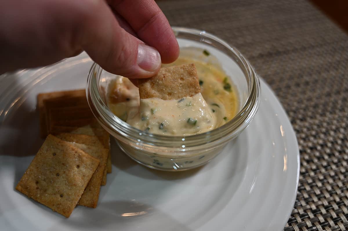 Sideview image of a hand dipping a cracker into the small bowl of dip.