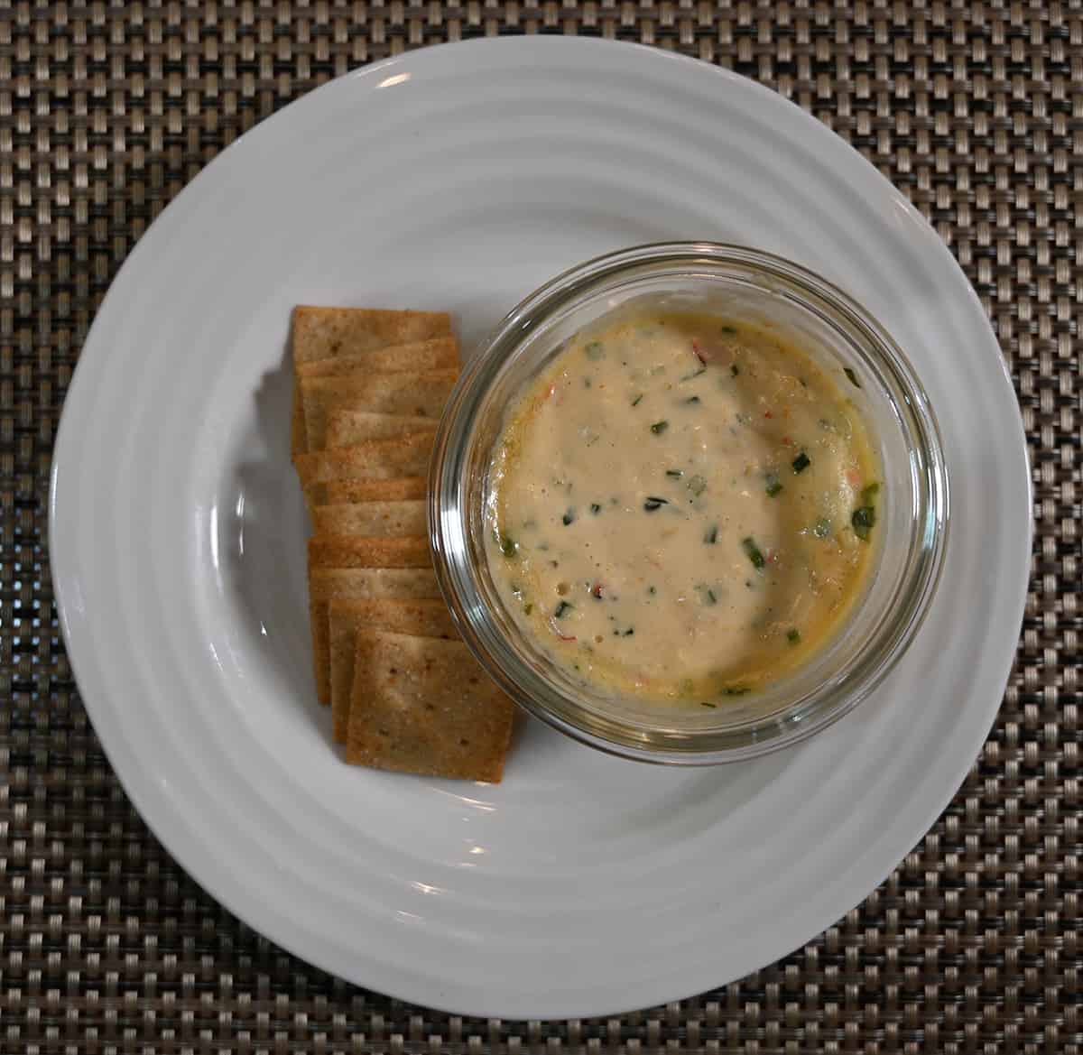 Top down image of a plate of crackers beside a small bowl of warmed smoked gouda & peppers dip.