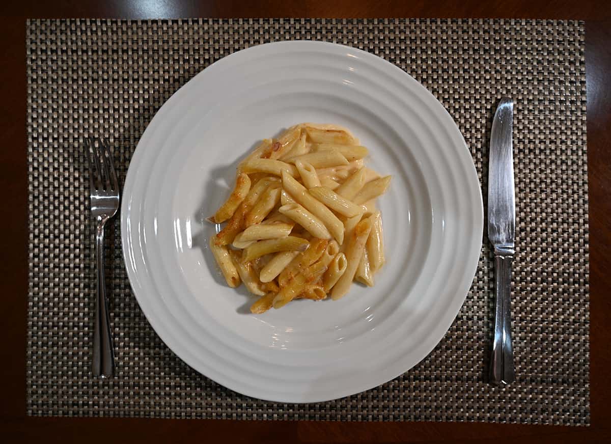 Top down image of white plate with mac and cheese served on it. Beside the plate is a fork and knife.