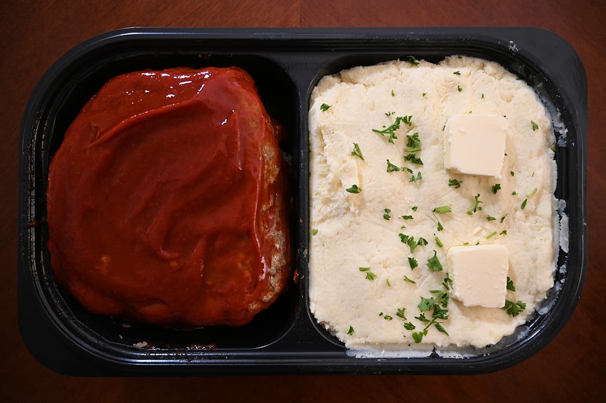 Top down image of the meatloaf and mashed potatoes container open so you can see the meatloaf and mashed potatoes. The potatoes have two slabs of butter on top.