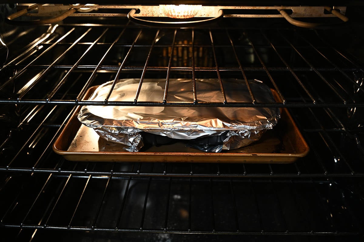 Image of a tray of mashed potatoes and meatloaf covered with aluminum foil sitting on a baking tray being baked in the ovven.