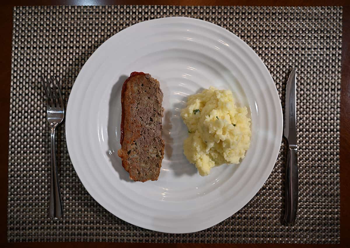 Top down image of a white plate with a piece of meatloaf beside a pile of mashed potatoes on it.