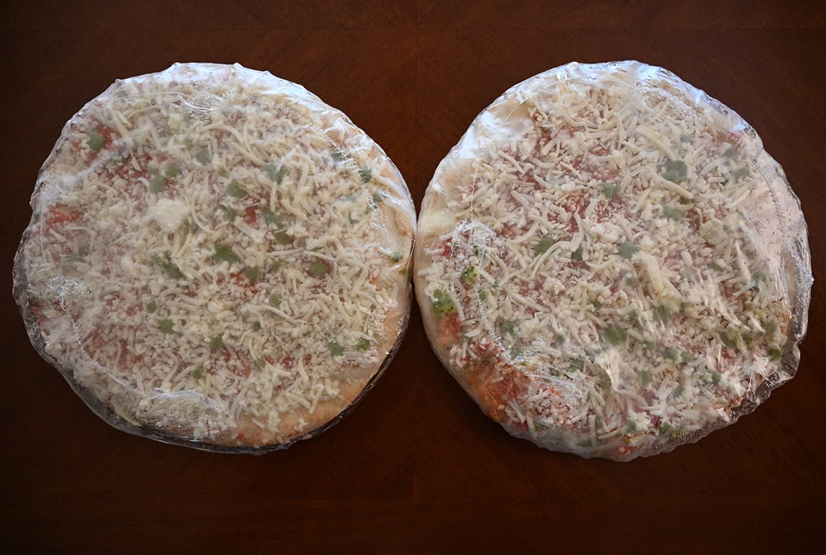 Top down image of two frozen pizzas individually wrapped in plastic sitting on a table.