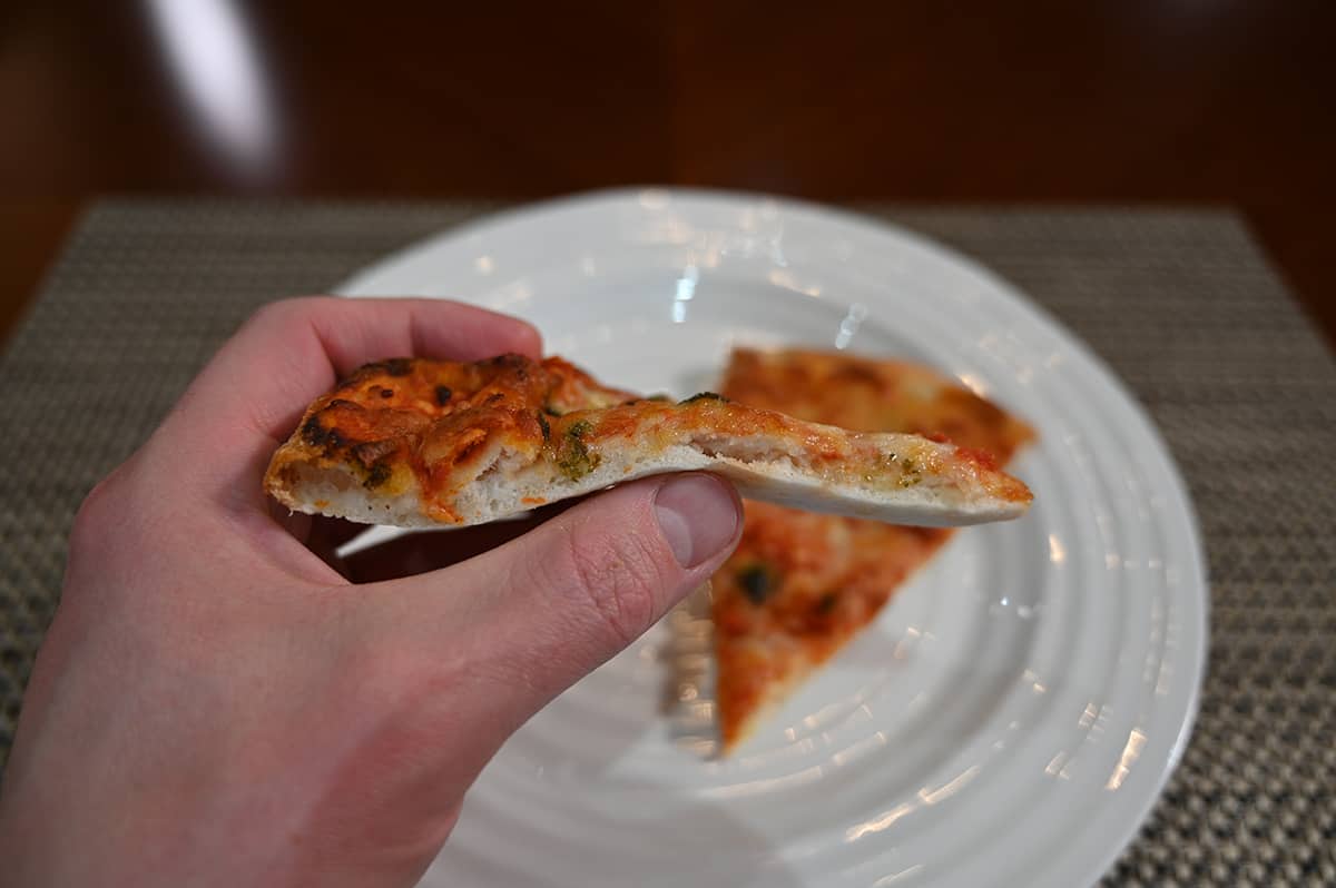 Side view image of a hand holding one slice of pizza up close to the camera so you can see depth of the crust clearly.