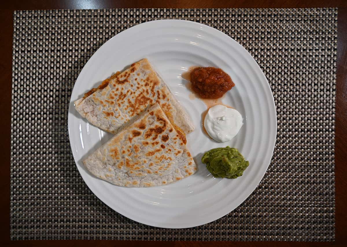 Top down image of a plate with two quesadillas on it with salsa, sour cream and guacamole 