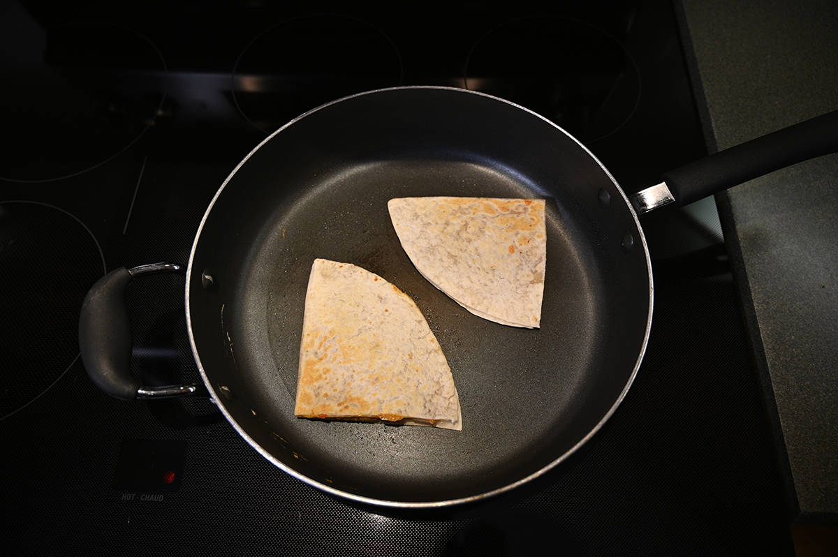 Top down image of two quesadillas frying in a pan.