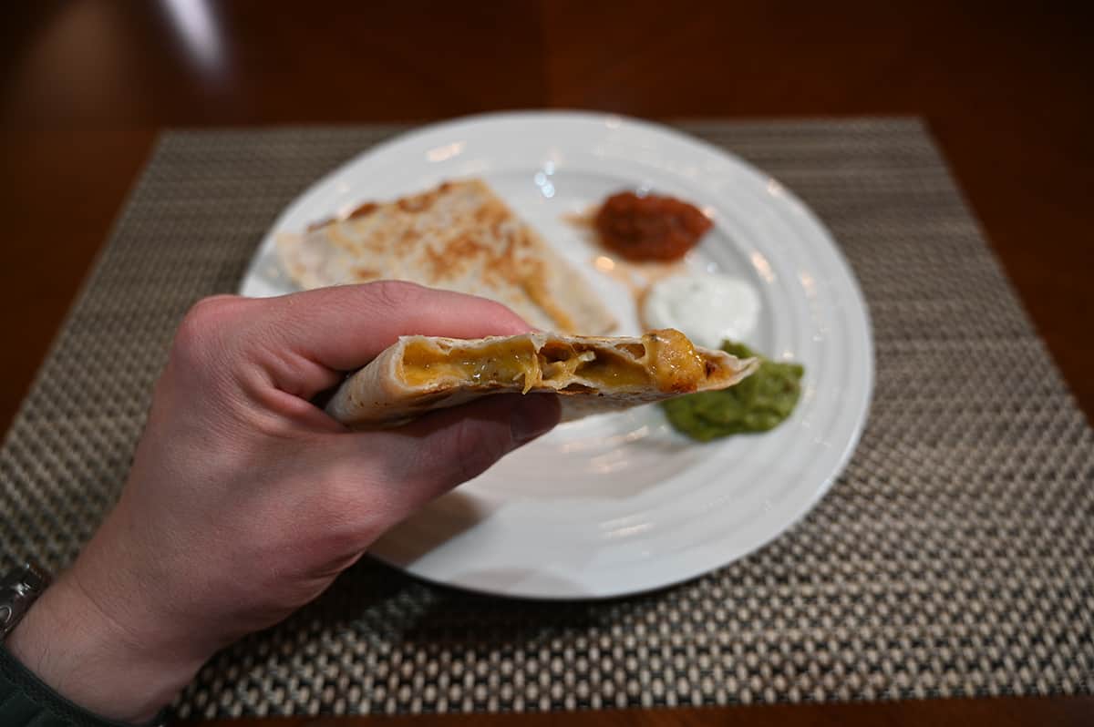 Closeup image of a hand holding a quesadilla with a few bites taken out of it so you can see the cheesy center.