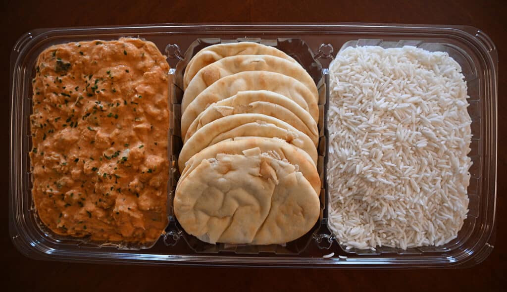 Image of the red thai chicken curry meal with the lid off sitting on a table. There is curry, naan and rice in three seperate sections.