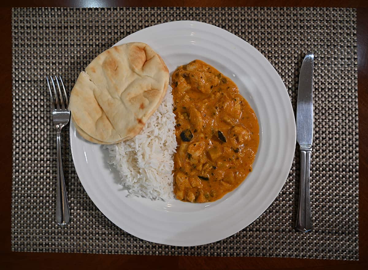 Top down image of a white plate with curry, naan and rice served on it.