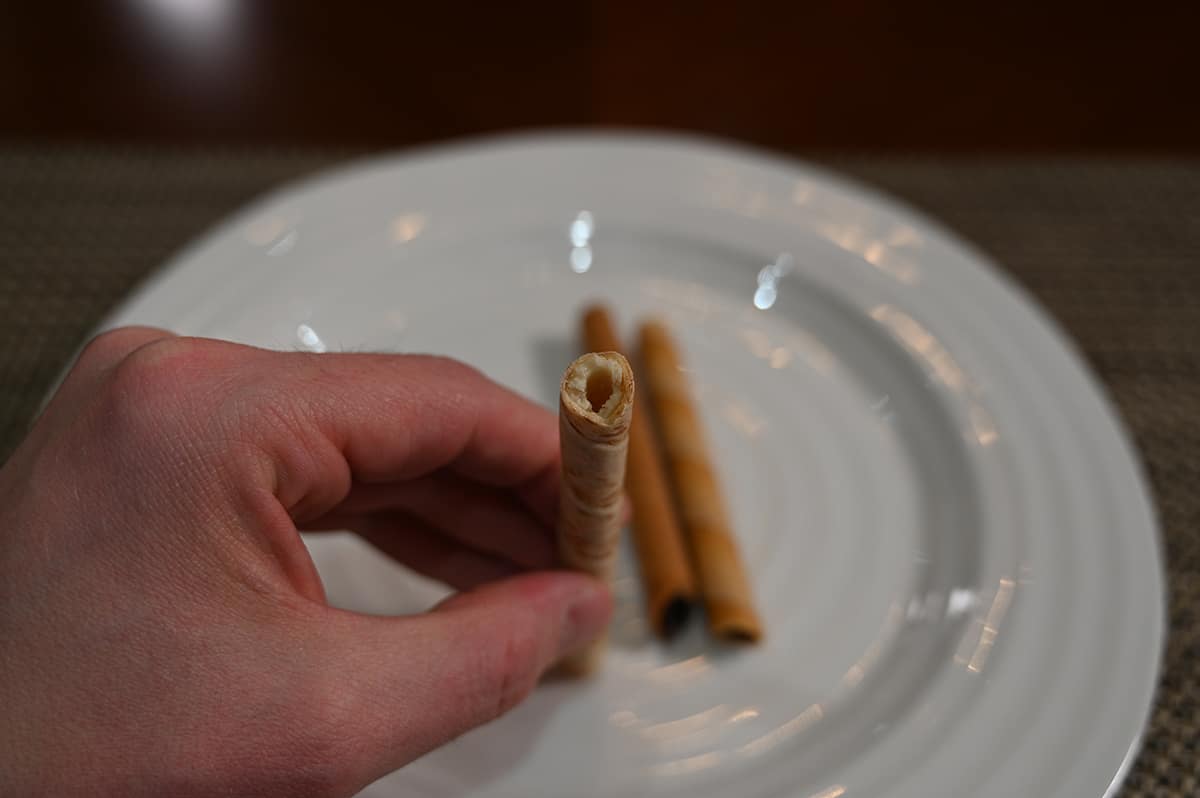 Top down image of a hand holding one vanilla rolled wafer up to the camera so you can see the filling inside.