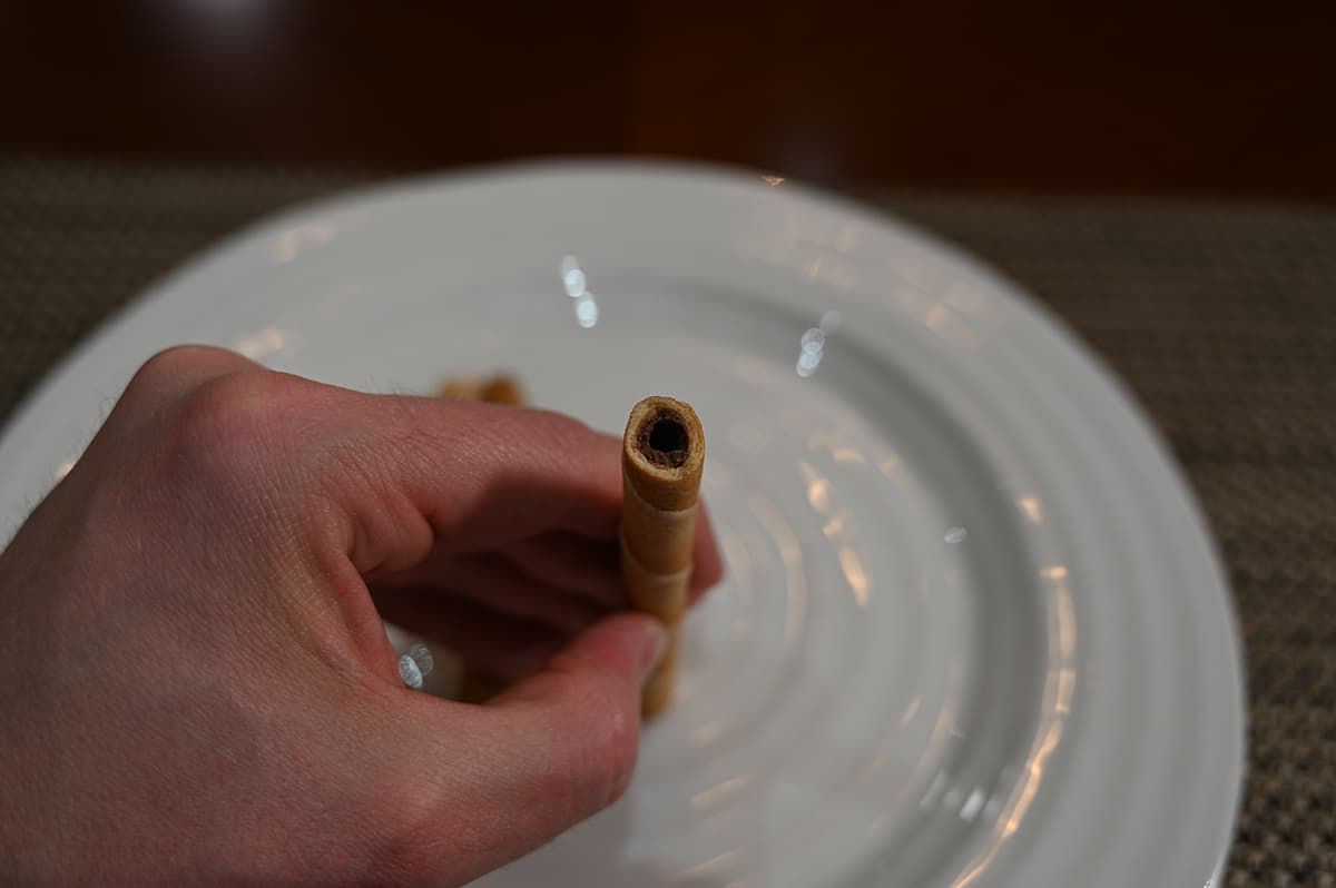 Top down image of a hand holding one hazelnut rolled wafer up to the camera so you can see the filling inside.