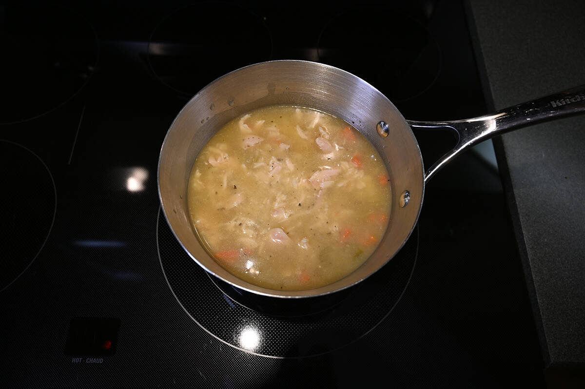 Top down image of a saucepan with chicken noodle soup in it cooking on the stove.