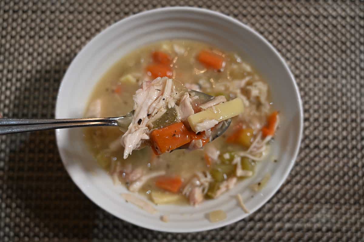 Closeup top down image of a bowl of chicken noodle soup with a spoon of it close to the camera.