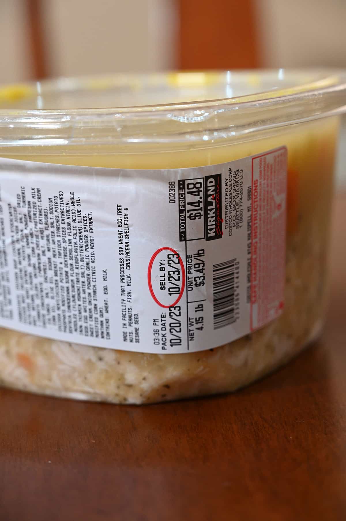 Closeup side view image of the container of chicken noodle soup showing ingredients, cost and best before date.