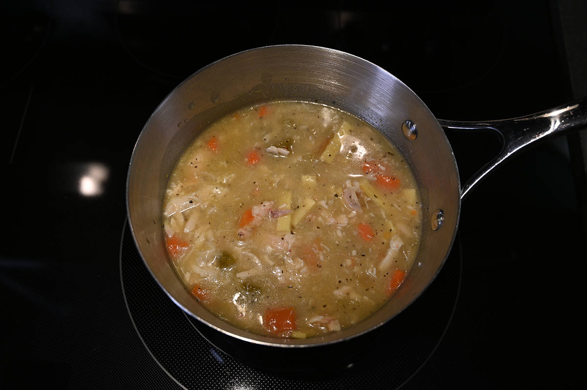 Top down image of a saucepan with chicken noodle soup in it cooking on the stove.