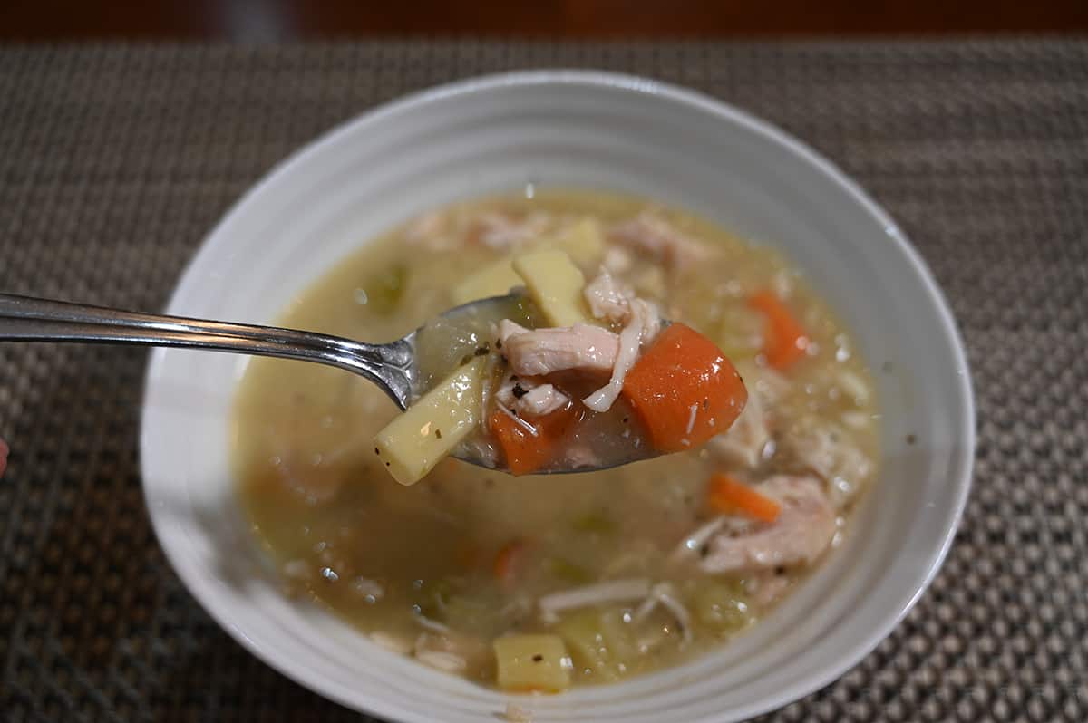 Closeup top down image of a bowl of chicken noodle soup with a spoon of it close to the camera.