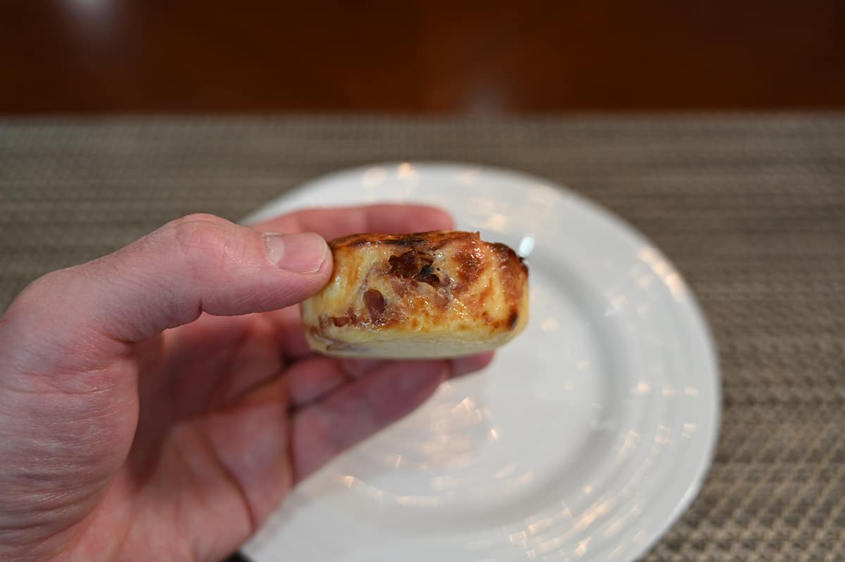 Side view image of a hand holding one egg bite close to the camera so you can see the side with a plate in the background