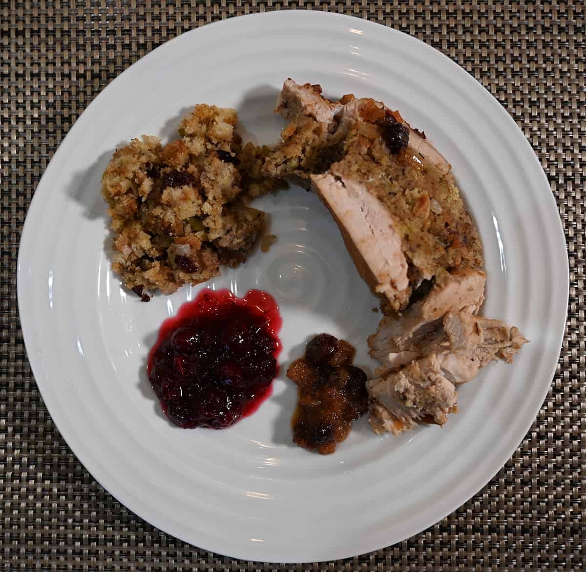 Top down image o a white plate with stuffing, turkey breast and cranberry sauce on it.