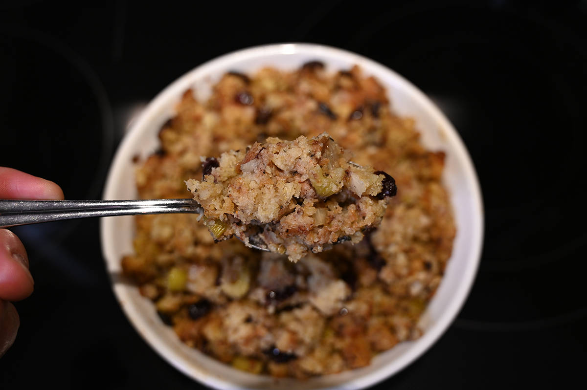 Top down image of a casserole dish full of cooked stuffing with a spoonful of stuffing hovering over the dish.