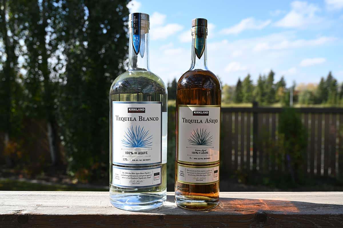 Image of the Costco Kirkland Signature Anejo and Blanco Tequila bottles sitting outside on a deck unopened.
